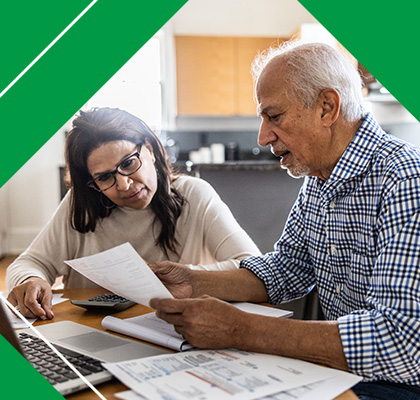 An older couple sitting at a table, reviewing financial documents and discussing their finances together.