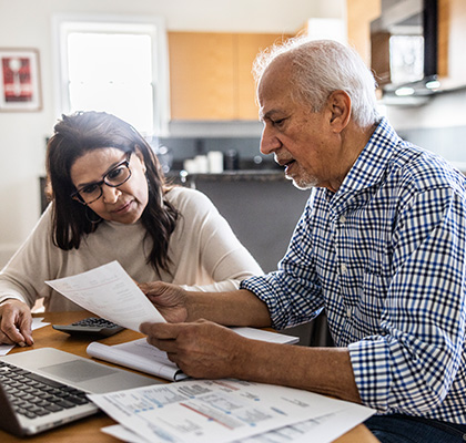 An older couple sitting at a table, reviewing financial documents and discussing their finances together.