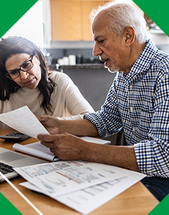 An older couple sitting at a table, reviewing financial documents and discussing their finances together.