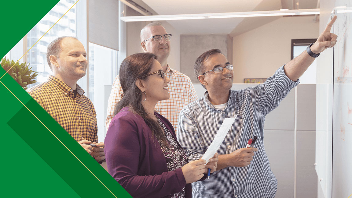 Four colleagues in an office looking and pointing toward something together.