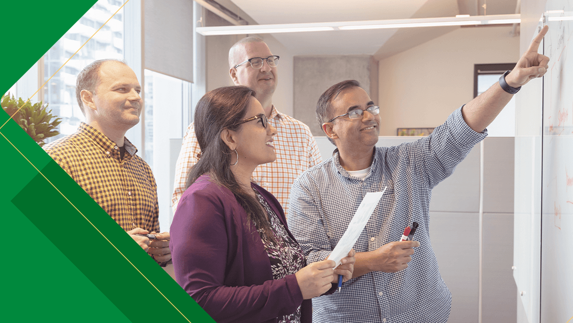 Four colleagues in an office looking and pointing toward something together.