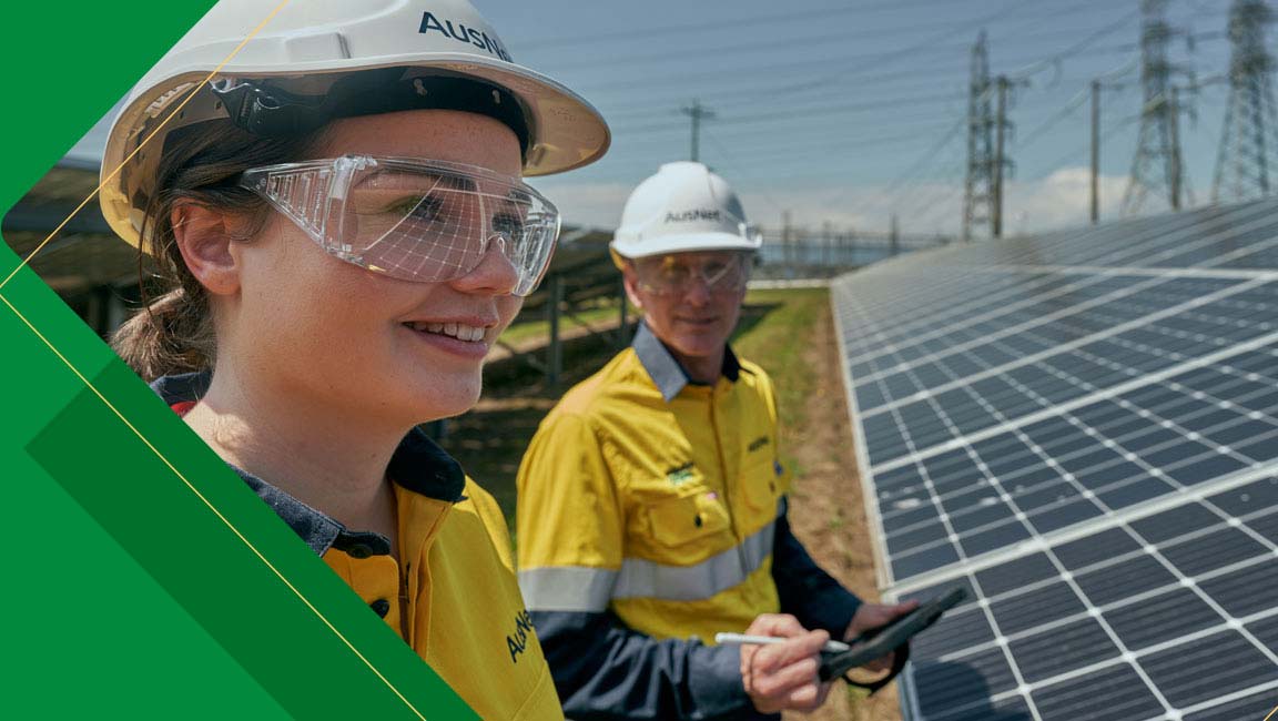 Two workers wearing hard hats and safety glasses standing beside solar panels.