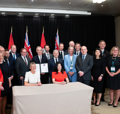 Canadian and Australian pension leaders pose in Sydney after signing an investment cooperation MOU, with both countries’ flags behind them.