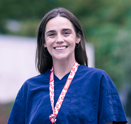 A smiling healthcare staff member wearing a lanyard outdoors.