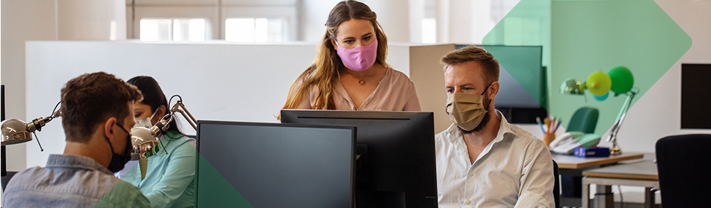 Employees wearing masks working together at desks in an office.