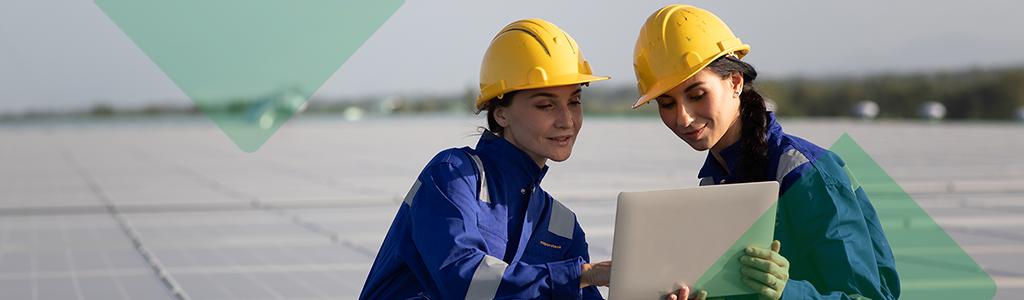 Two workers in hard hats reviewing a laptop at a solar site.