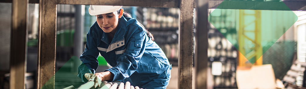A worker in protective gear handling pipes in an industrial setting.