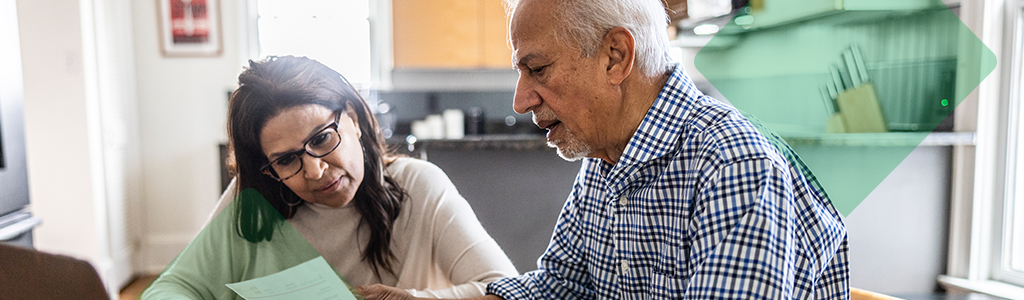 An older couple reviewing paperwork together at a kitchen table.