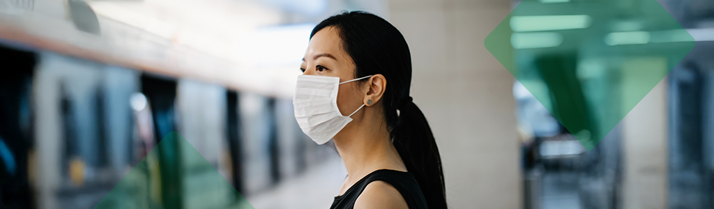 A woman wearing a face mask standing on a transit platform.