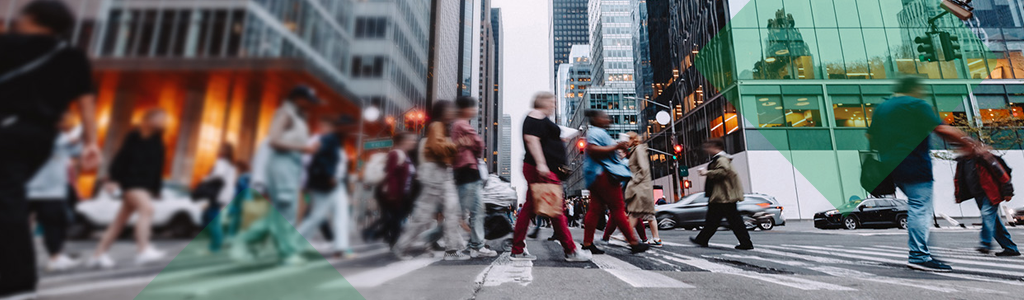 People crossing a busy city street between tall buildings.