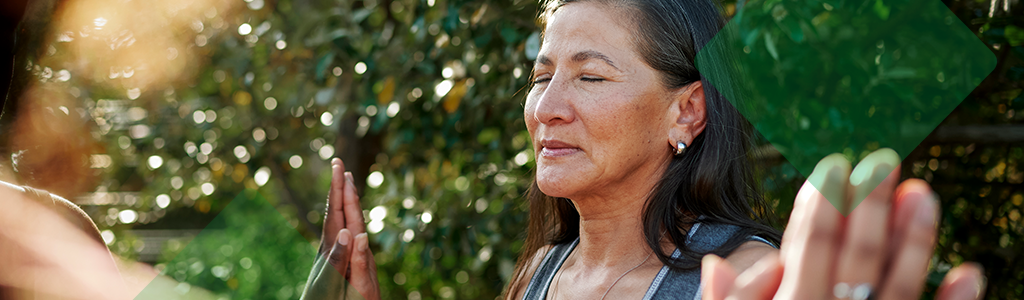 A woman practising mindfulness outdoors with her eyes closed.
