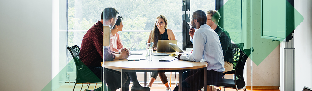A group of colleagues meeting around a table in a bright office.